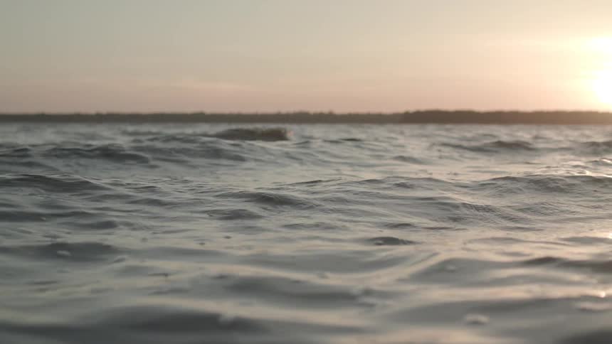 Sun shines from a red tinted sky onto shallow waves flowing across the surface of the water