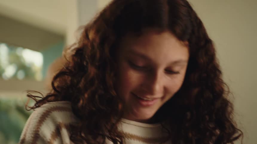 A young girl stands in the kitchen laughing joyfully as she prepares food