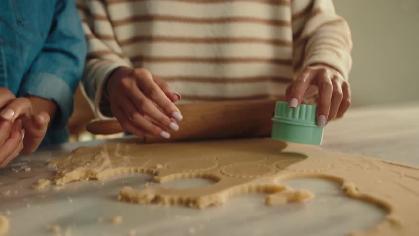 Two young women are using a round utensil to cut pieces of shortbread cookies that are on a flat table