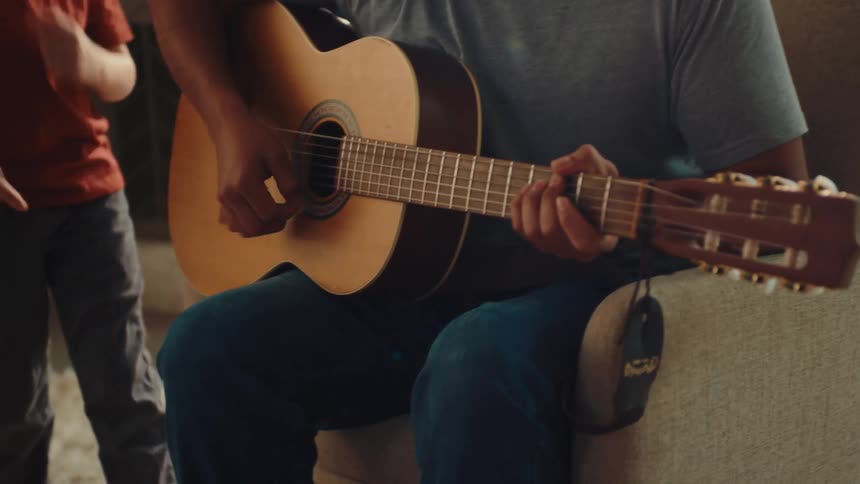 A boy is dancing while his father plays guitar
