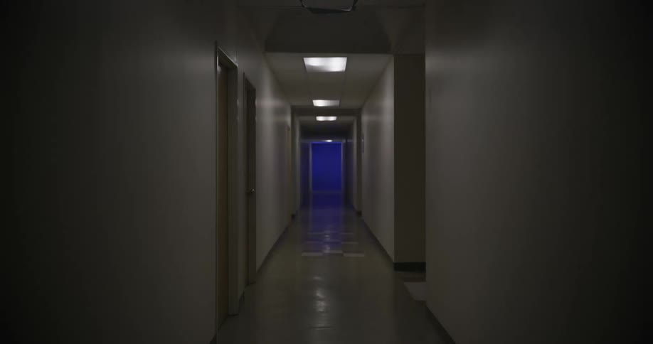 A dark hallway is illuminated by overhead lights and a blue light at the far end