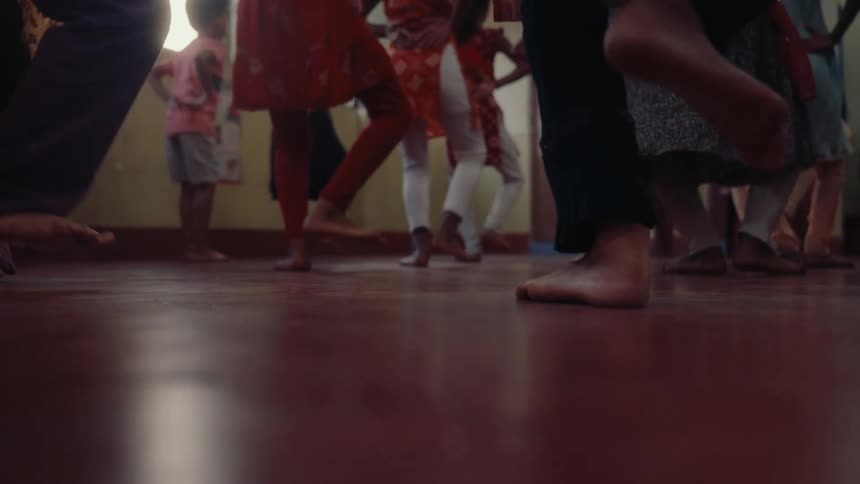 Barefoot children practice indian dance in a classroom seen from a low angle