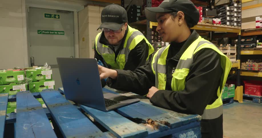 Two workers are talking in the warehouse while looking at a laptop