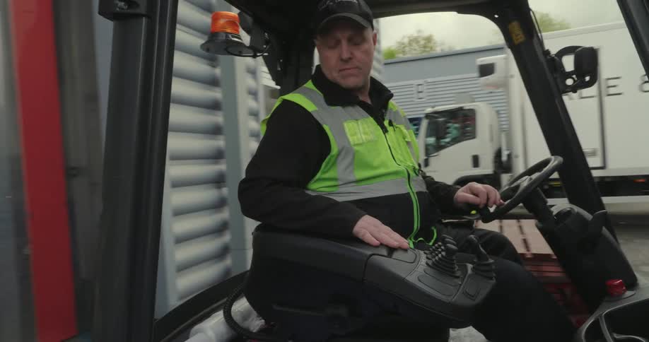 A man backs a forklift up to the opening of a warehouse