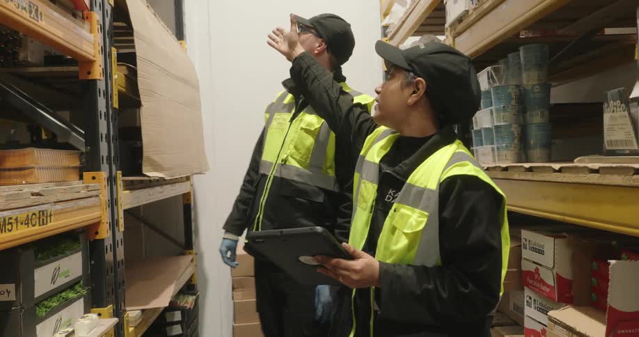 Two warehouse workers review inventory on a tablet in a warehouse aisle
