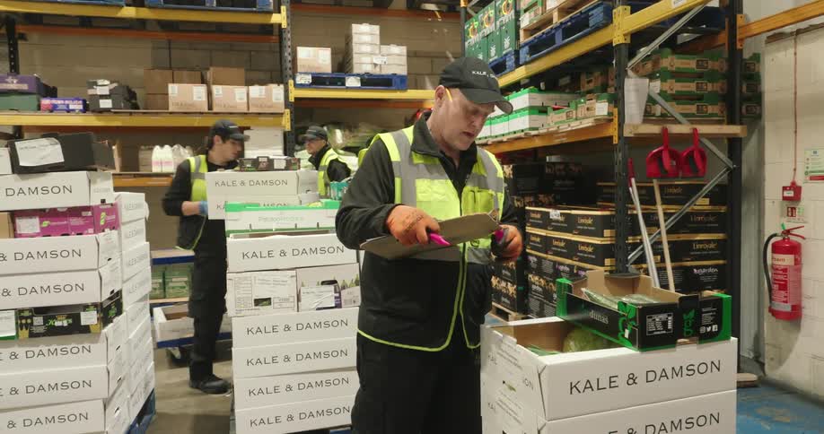 A group of workers actively organize and sort packages in a busy warehouse with stocked shelves towering around them
