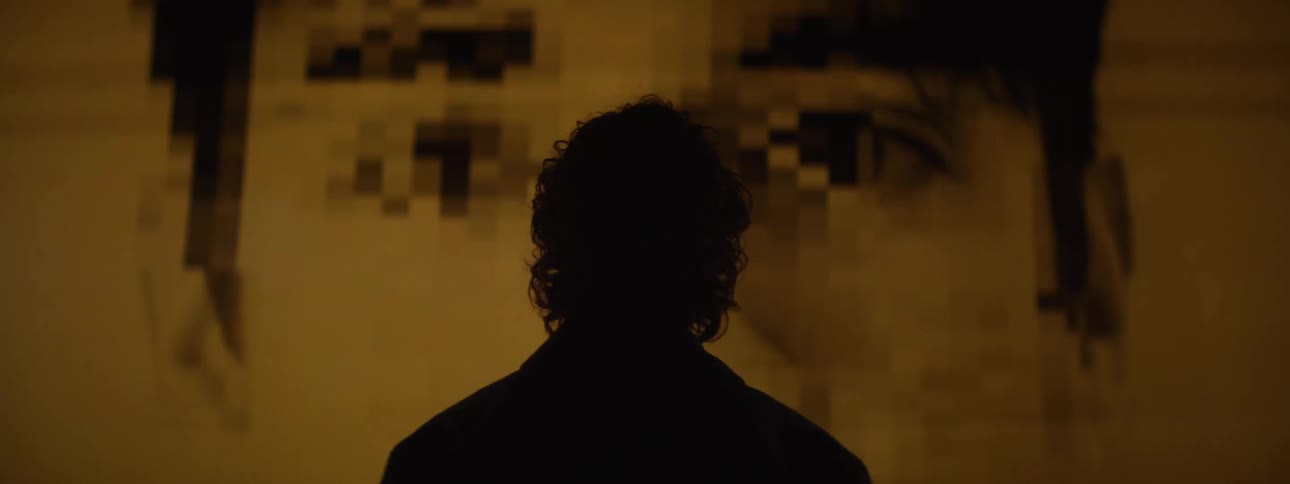 A silhouetted figure faces a large projected image of staring eyes