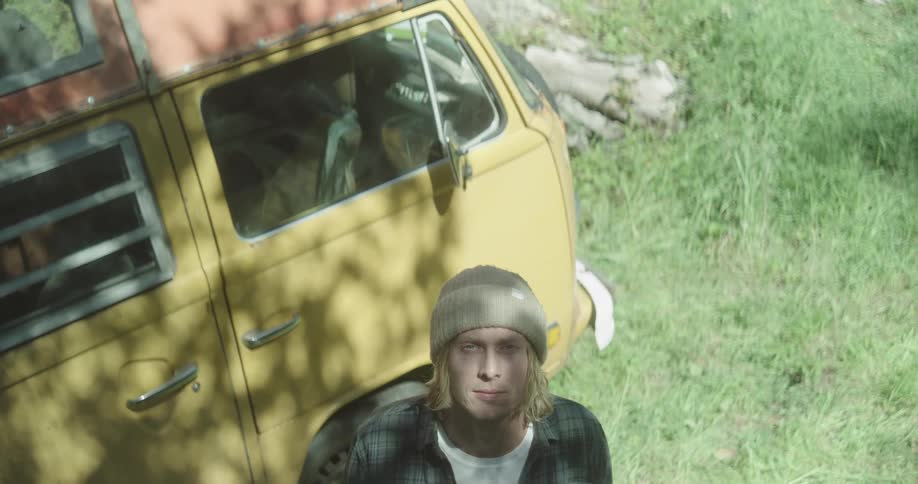 Man in a beanie looking up next to a colorful kombi van outdoors