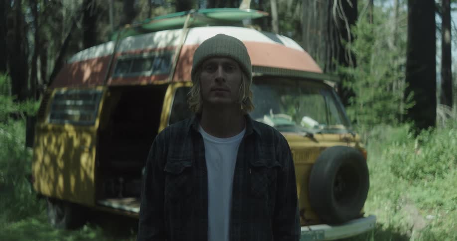 A man is standing in front of his van in the woods