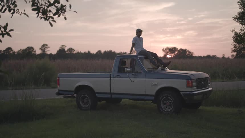 Man sitting on top of a pickup truck in a field in the late afternoon