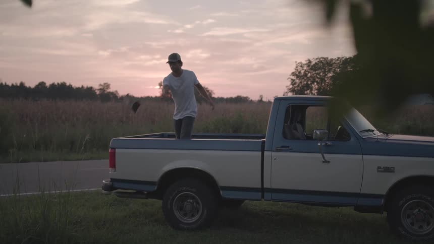Man unloads firewood from a pickup truck parked across from a crop field