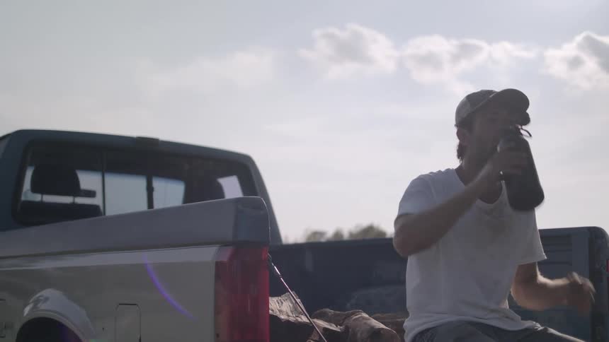 A man drinks from a thermos while sitting on the bed of his truck