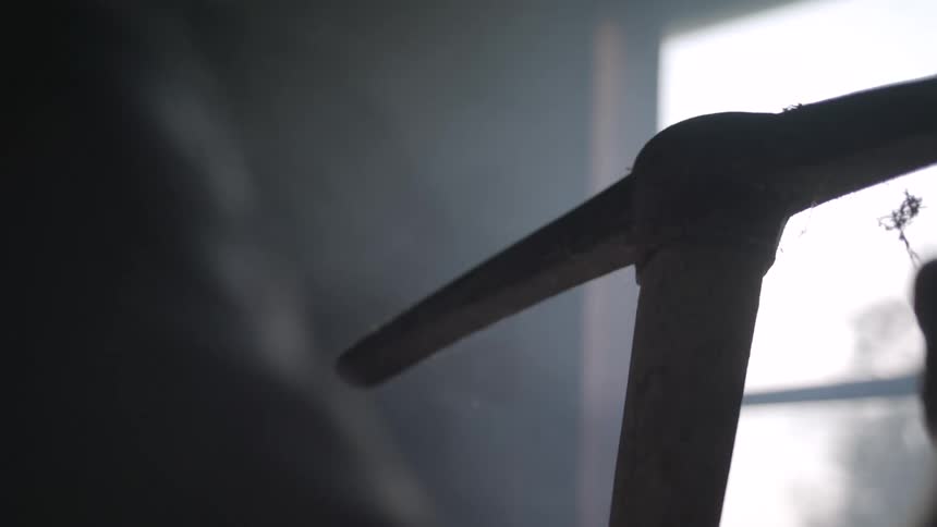A person examines a worn dirtcovered pickaxe in a dimly lit room
