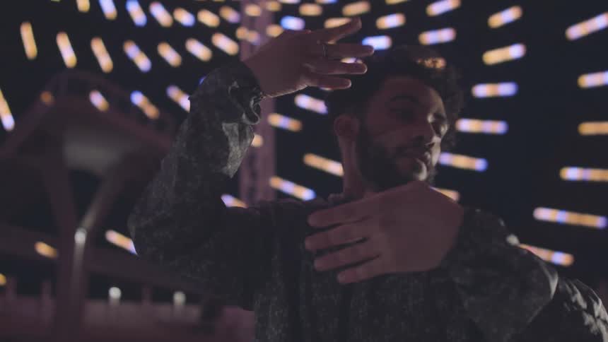 A man performs on stage dancing with expressive hand gestures and smooth flowing body movements