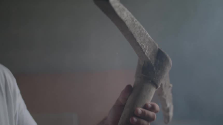A person examines a worn dirtcovered pickaxe in a dimly lit room