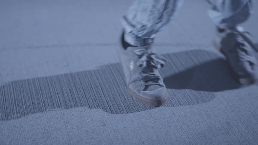 A young man wearing shoes is doing leg dancing with the rooms light casting his shadow on the floor