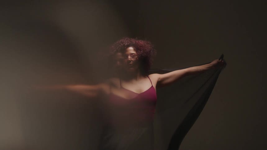 Woman wearing a dress holds a thin wrap behind her as the air stirs it and her hair