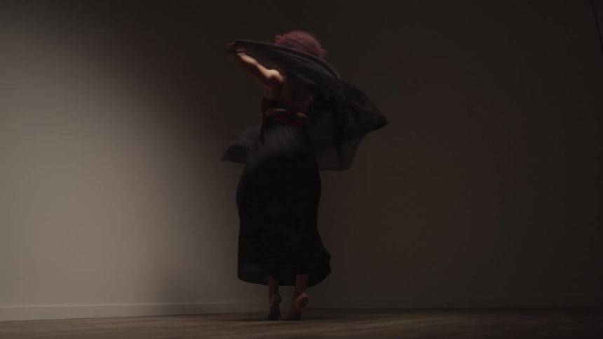 A woman is dancing wearing a flowing black skirt and a maroon top with a piece of black fabric trailing behind