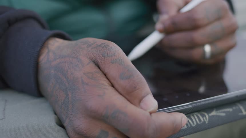 A mans hands hold a tablet while he writes on it with a stylus