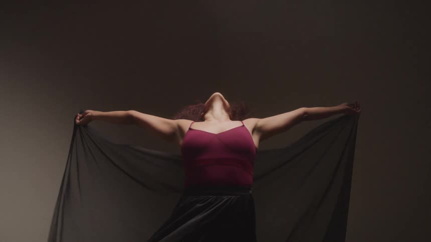 A female dancer reaches back and stretches with a black scarf draped behind her