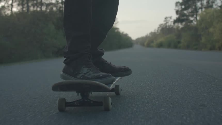 Legs of a person skateboarding on a paved road surrounded by vegetation
