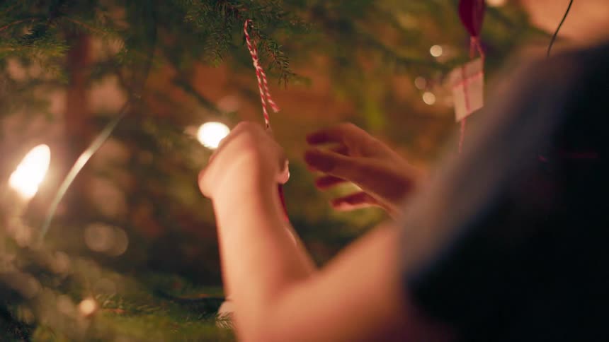 Child placing a decoration on a christmas tree with lights