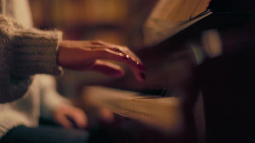 A female wearing a winter sweatshirt sitting indoors while playing the piano