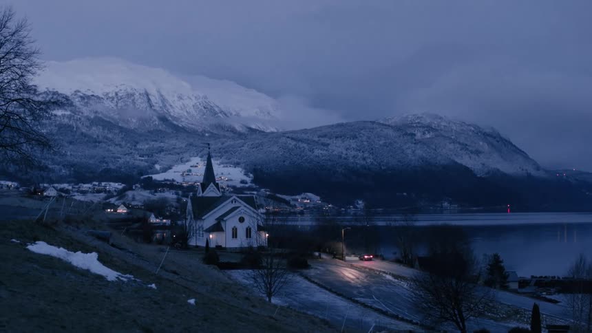 Car drives past a church in a waterside town on a winter evening