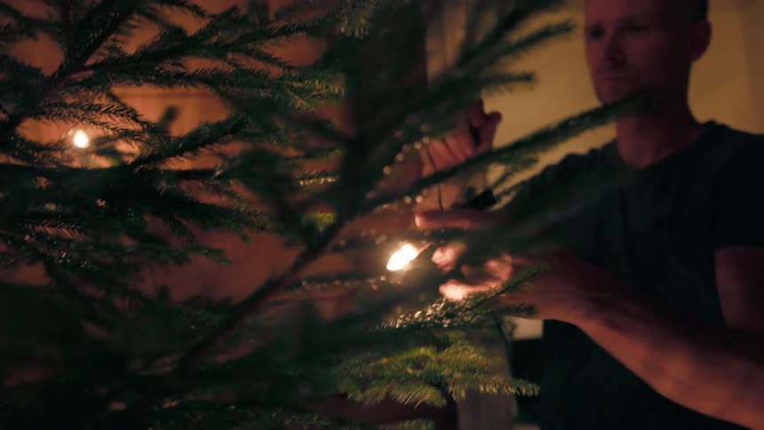 A man strings lights on a tree while a child skips in the background