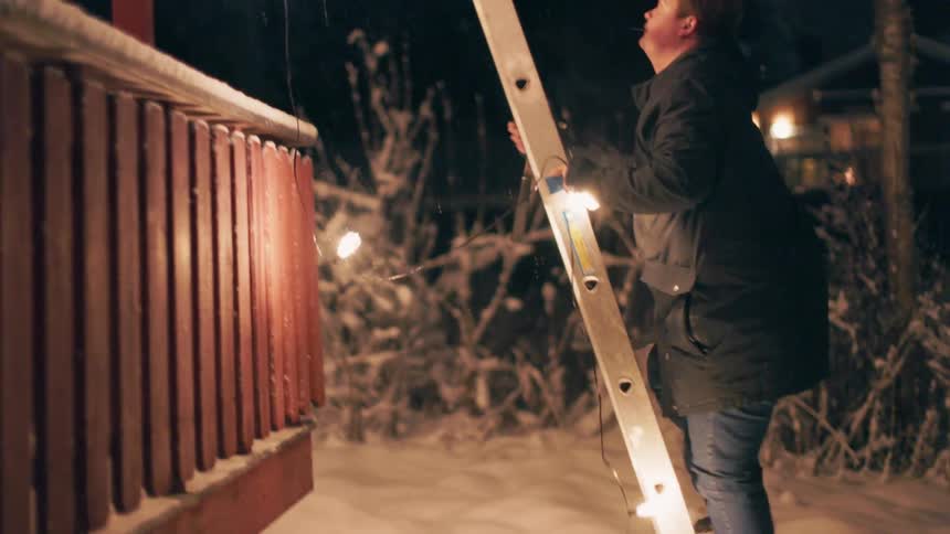 A man is climbing a ladder while installing christmas lights on the roof