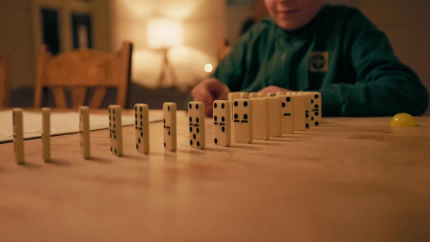 A boy is stacking dominoes in a line