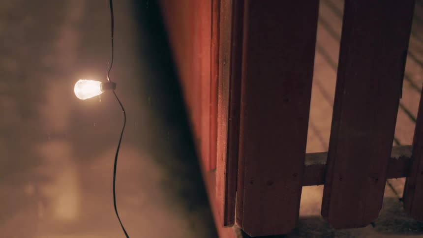 Lit light bulb hanging from a decorative string outside a house on a snowy night