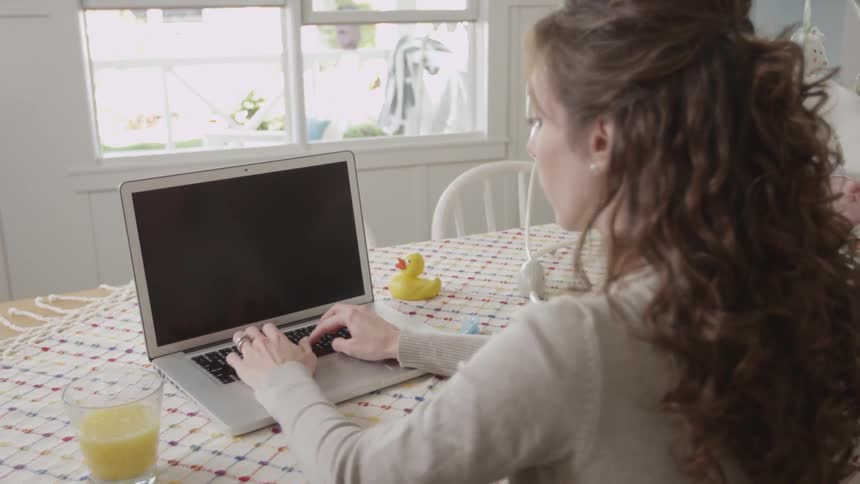 Woman works on laptop beside a baby in a swing
