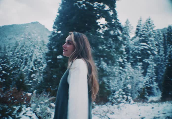 A woman is walking in the snow by the trees on the mountain
