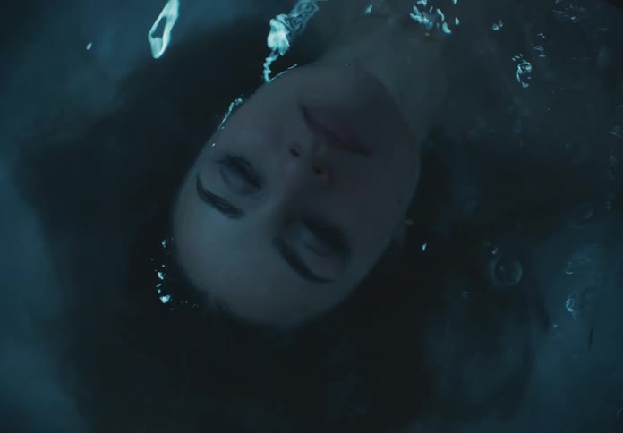 The face of a woman lying in the water with her hair underwater and her eyes closed