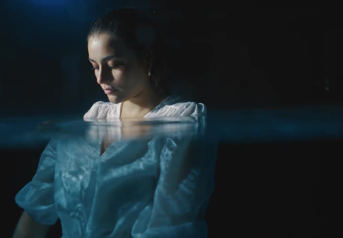 A woman who is partially underwater wearing a white outfit in a dark environment