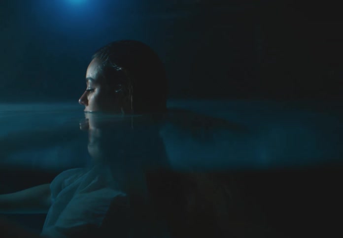 Woman in white dress partially submerged in water in a dark environment