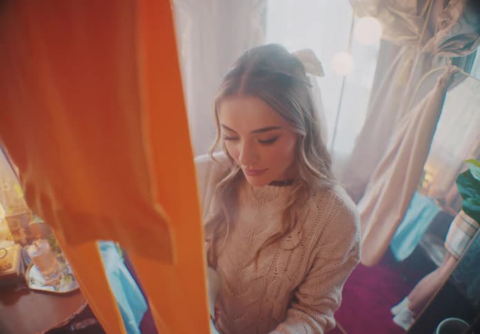 The face of a young blonde woman who is using a hot steam iron on an orange garment