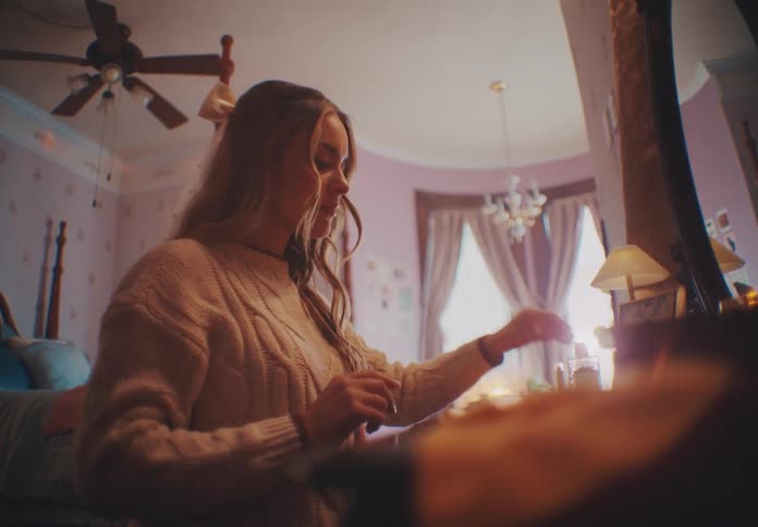 The face of a woman who is taking an object that is on her table and placing it on the other side and she is in a room with pink walls