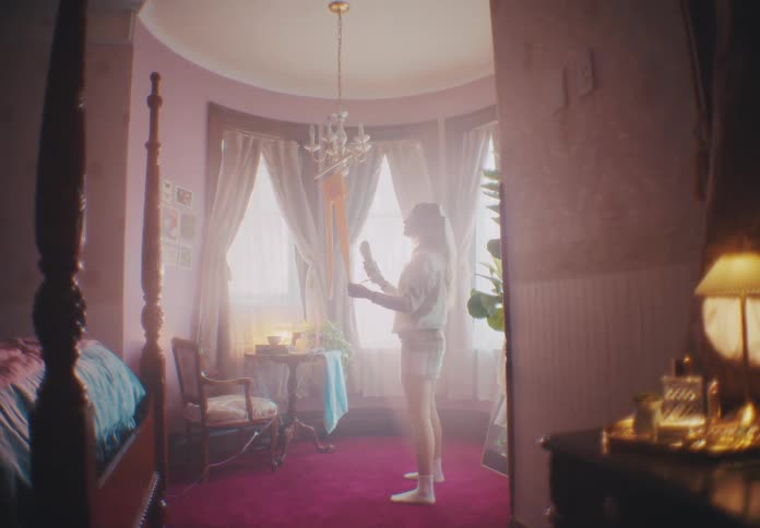 Woman entering a room hanging up a pair of pants and ironing them with a hot iron
