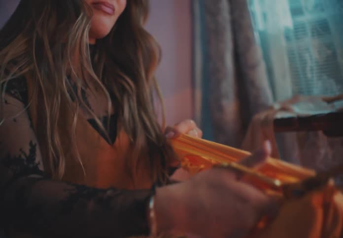 A young female takes off a piece of cloth picks up a pair of scissors and angrily cuts it into several pieces while in her room at midday