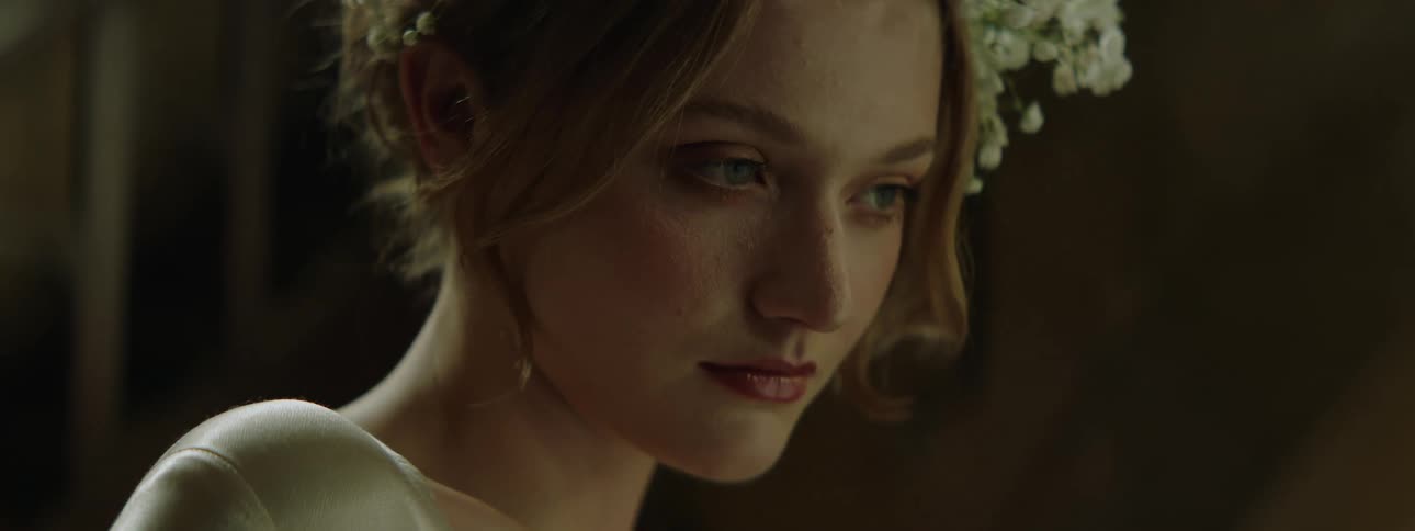 A contemplative young woman with flowers in her hair is softly lit in a closeup shot