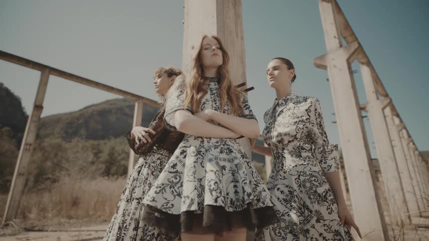 Three models stand and pose beside a pillar in a roofless ruined building on a sunny day all wearing identical clothing