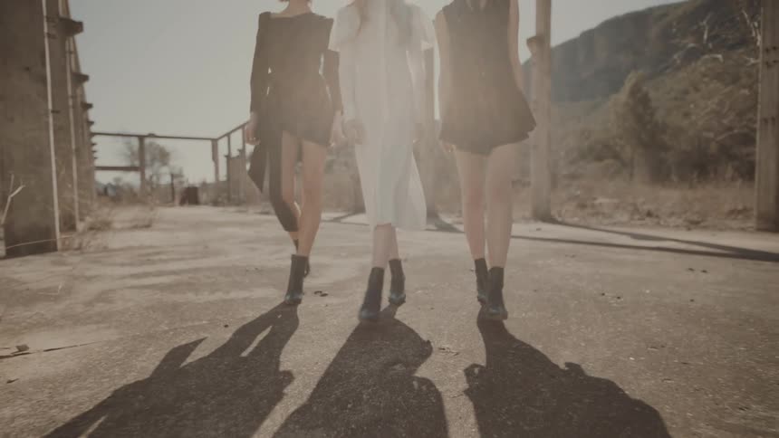 Three female models in dresses walking in an unfinished structure with mountains in the background