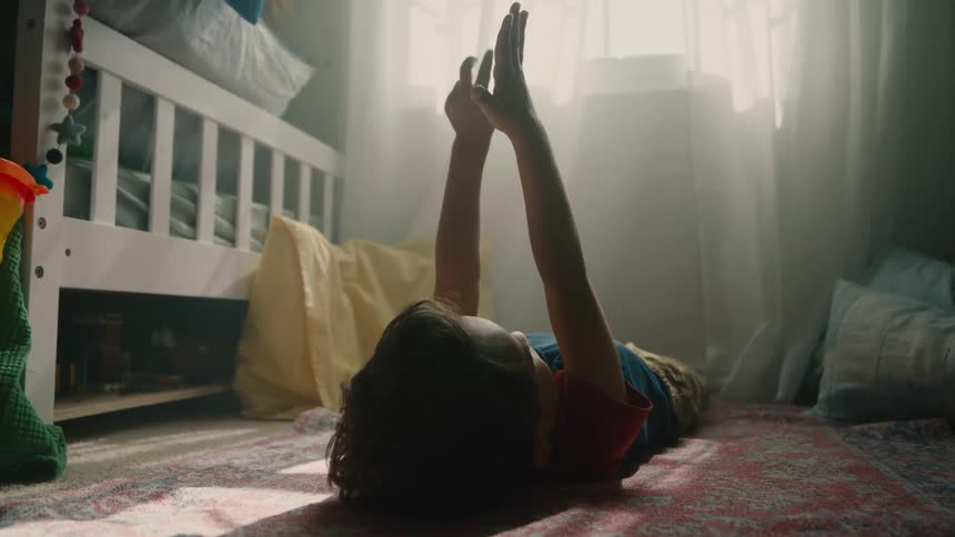Boy lying on the carpet in a room with his hands raised up