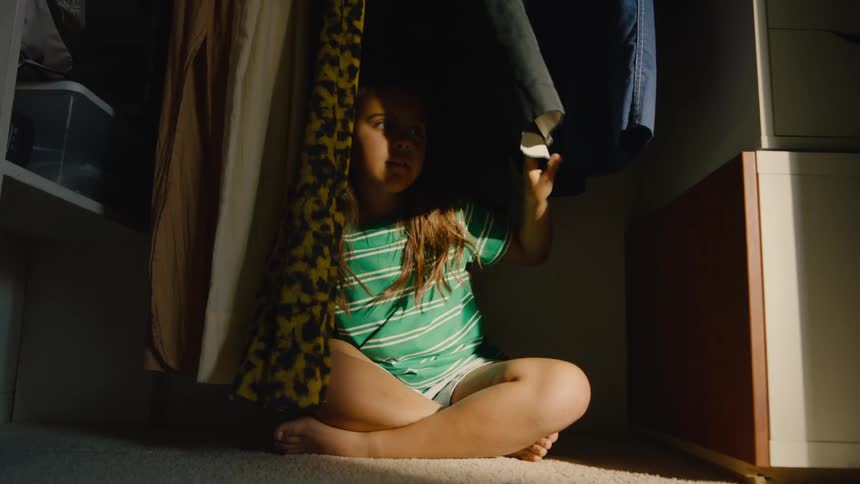 A child hiding among clothes in a closet