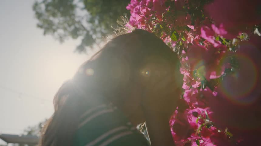 A young girl covers her eyes while playing hide and seek beside a vibrant pink flower bush in bright daylight