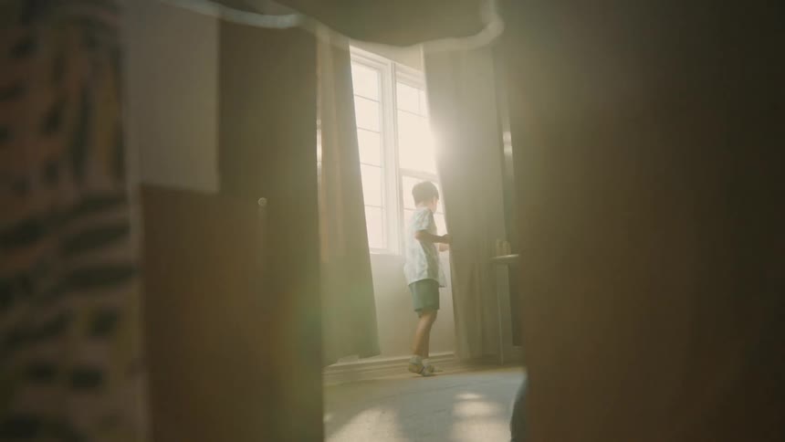Boy looking for something behind the curtains of a window