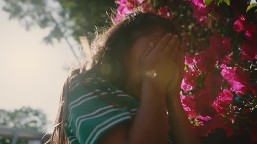 A girl faces the flowers and coves her face while counting