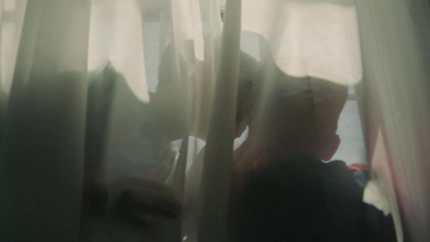 Two kids play behind sheer curtains silhouetted by daylight through a window